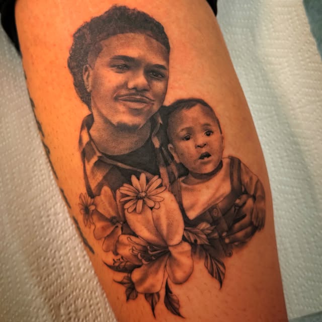 Black-and-grey memorial portrait tattoo of an adult holding a baby