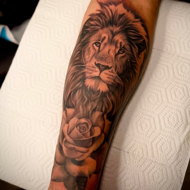 Detailed black-and-grey lion and rose tattoo on a forearm